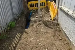 Trench for the new water main with site barriers in place alongside the building